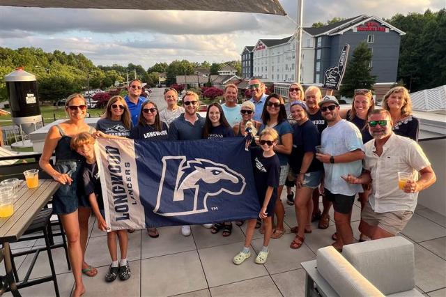Longwood alumni and families gather at a regional event while holding a Longwood Lancers flag.