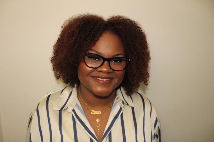A woman in glasses and a striped blouse smiles for a headshot against a plain light background.
