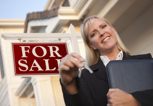 Real estate agent with keys in front of a house with a For Sale sign