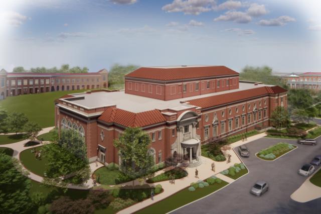 Aerial rendering of a red-brick academic building with a terracotta roof. The building features arched windows, decorative stonework, and a central entrance. Landscaped walkways, trees, and small groups of people surround the structure. Additional campus buildings and green lawns appear in the background under a blue sky.