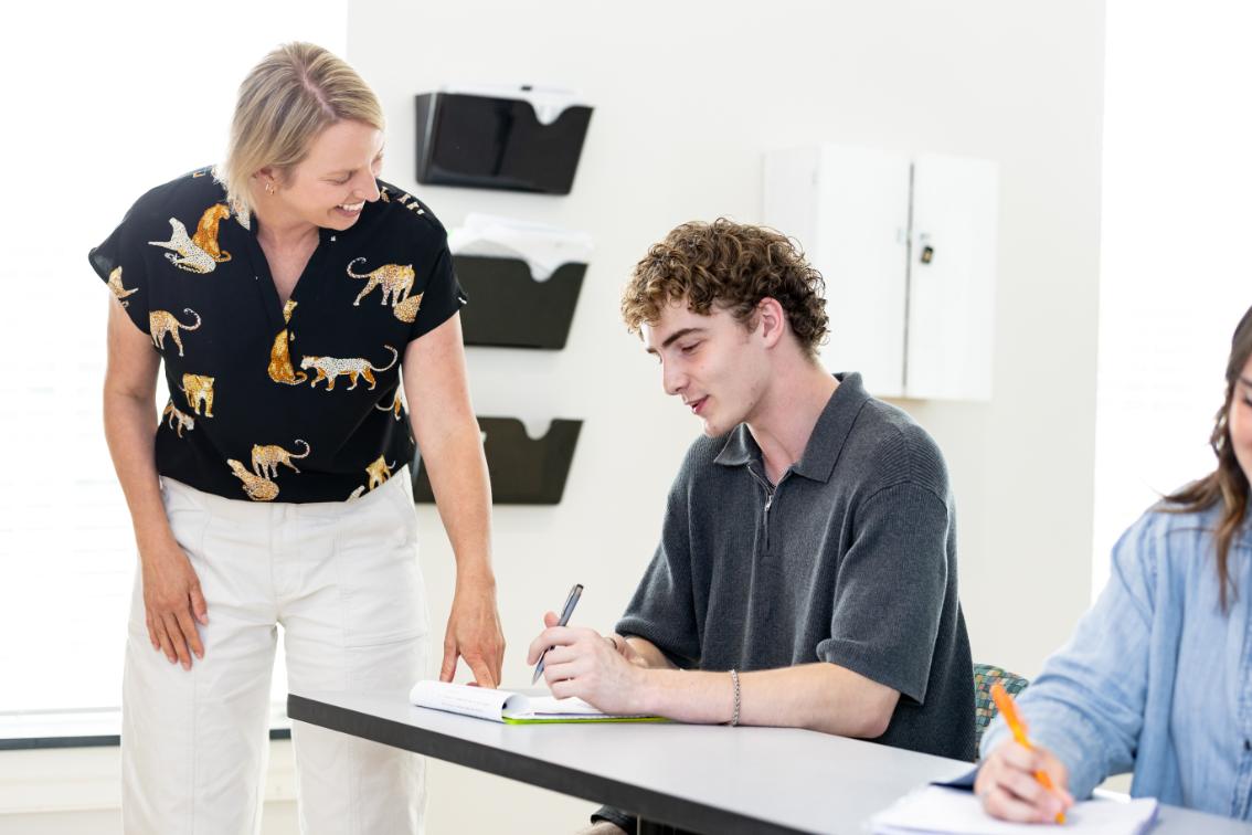 A Longwood faculty member smiles while helping a student with notes during a classroom discussion.
