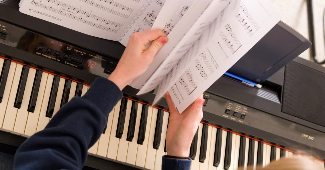 Student at a piano flipping through a music book