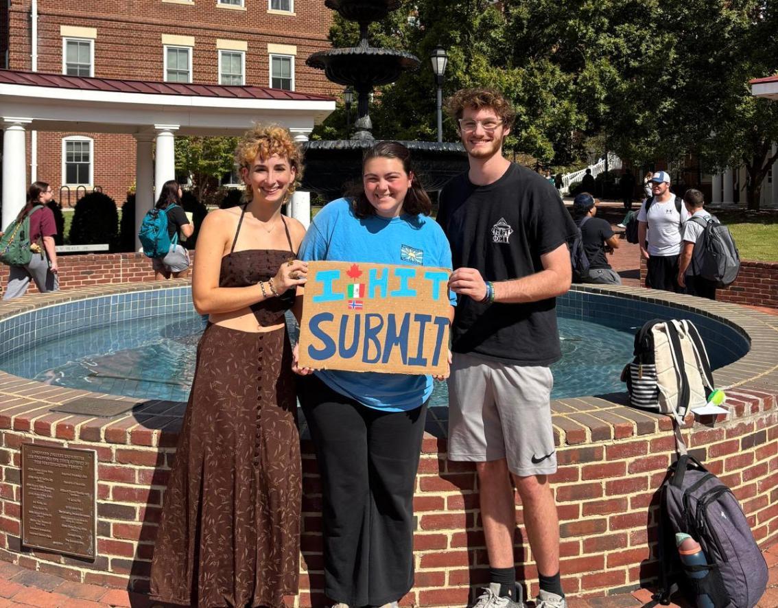 Left to right, Sarah Gressett '26, Kara Burks '26 and Ryan Urban '26 pose with a sign that reads 
