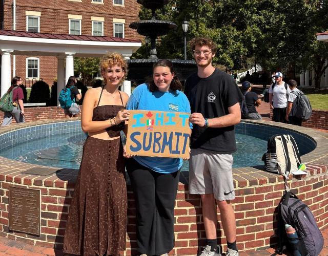 Left to right, Sarah Gressett '26, Kara Burks '26 and Ryan Urban '26 pose with a sign that reads 