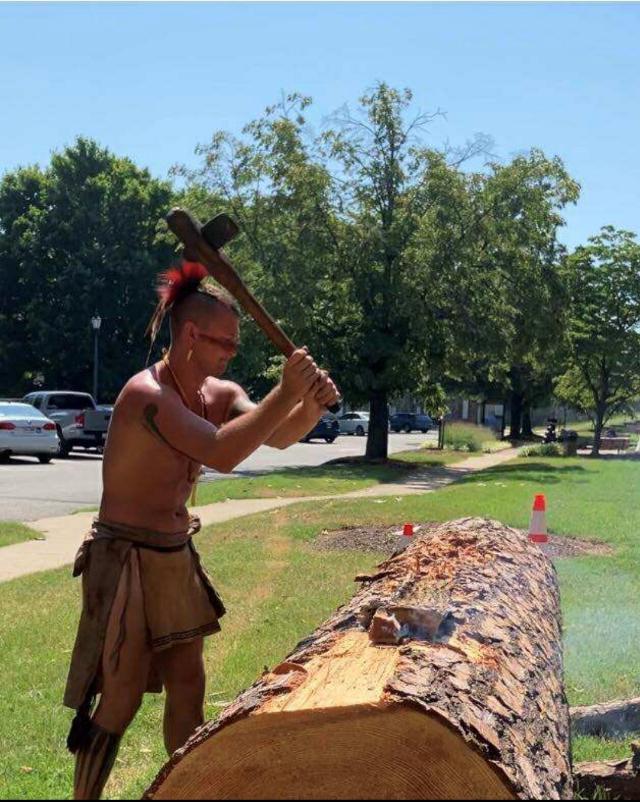 Russell Reed is cutting into a log with his axe, recreating the Native American art form of canoe making