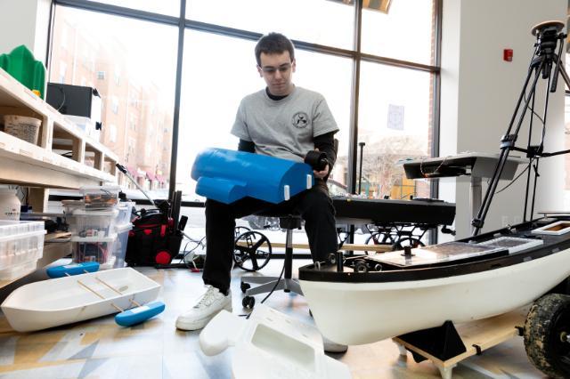 Senior Ben Gettier works on a portion of his nautical device in Longwood's SEED Innovation Hub. He is sitting in front of a window, on a rolling chair, holding two parts to the device.