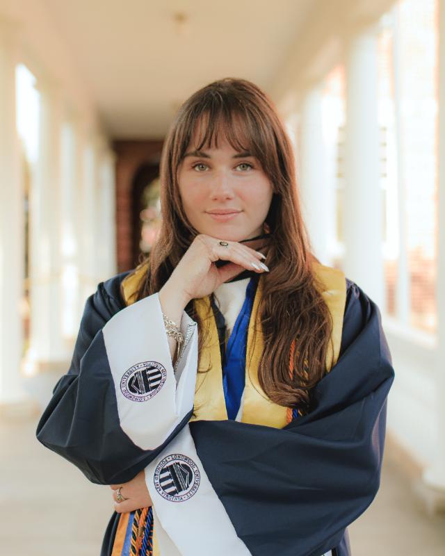 Photo of Megan Brown in her Commencement regalia, standing in Longwood's iconic colonnades.