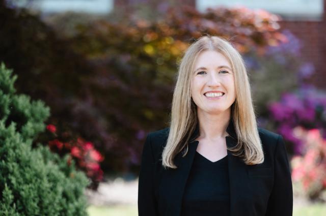 Headshot of Dr. Tai Johnson, assistant professor of history, standing in front of the colorful, flowering bushes that adorn the front of Eason Hall.
